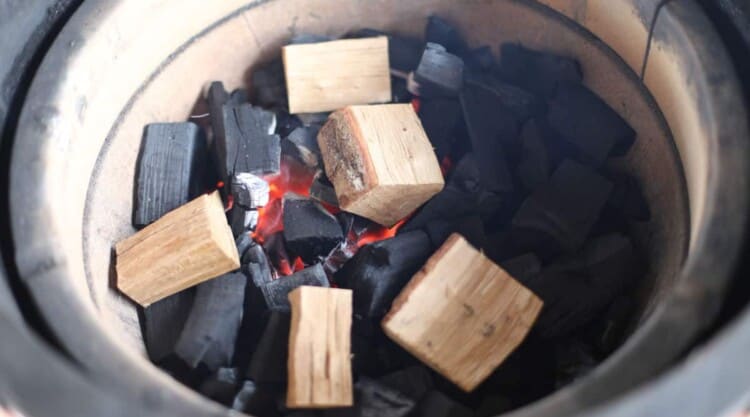 Close up of a Kamado Joe fire bowl filled with lump charcoal and smoking wood.