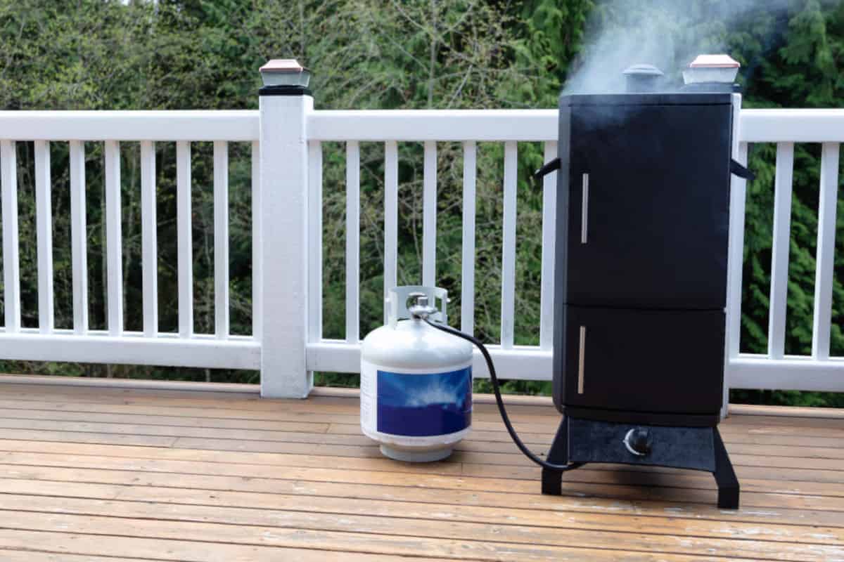a propane gas smoker on a wooden balcony with LP tank beside it