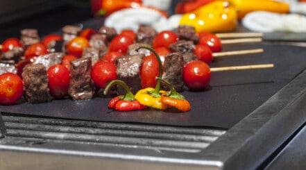 Close up of some mixed meat and veg kabobs on a grill mat.