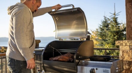 Man lifting lid on a camp chef pellet smoker, inspecting his BBQ brisket