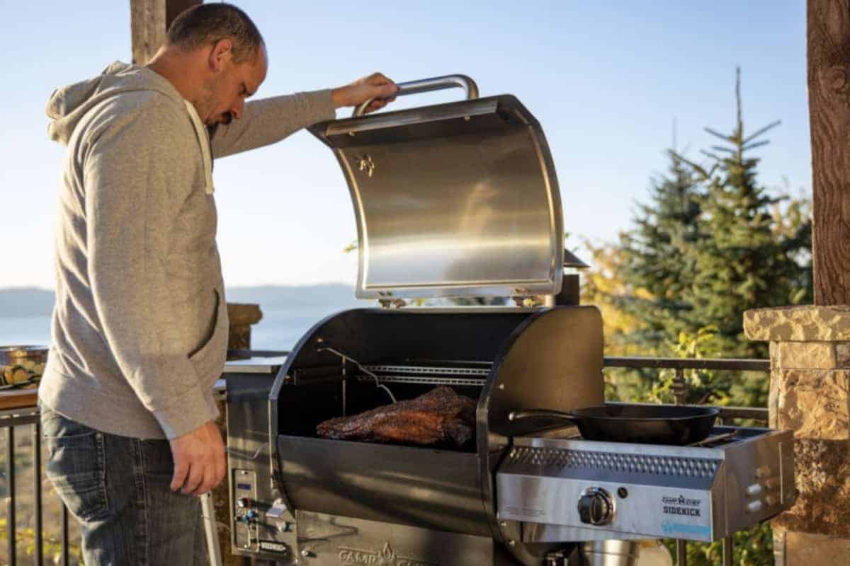 Man lifting lid on a camp chef pellet smoker, inspecting his BBQ bris.