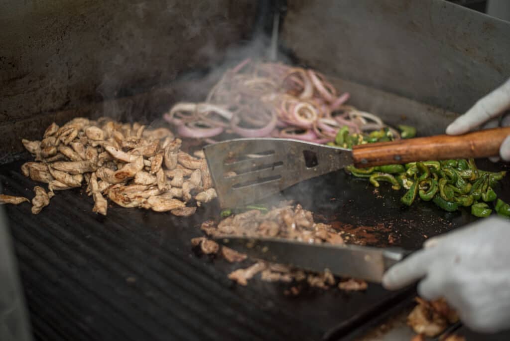 Chopped onions, mushrooms and chilies being fried on a grill mat on a gas grill