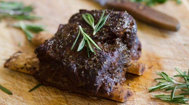 Beef ribs on a cutting board with a few rosemary leaves.
