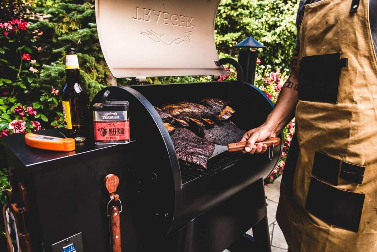 traeger pro series 22 in use by a man with an apron, with the lid open and the grill full of f.