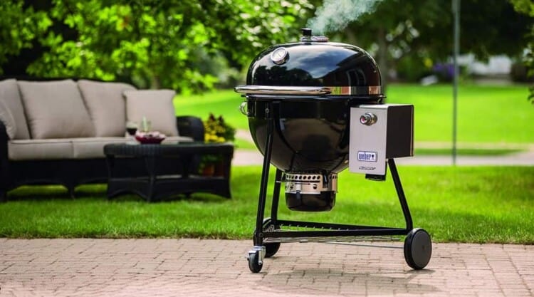 Weber summit charcoal grill on patio, near grass garden with sofa in background.
