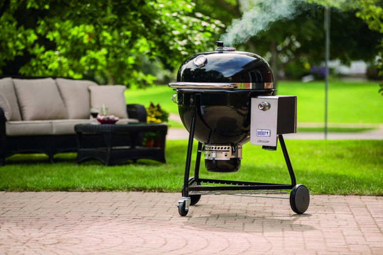 Weber summit charcoal grill on patio, near grass garden with sofa in background