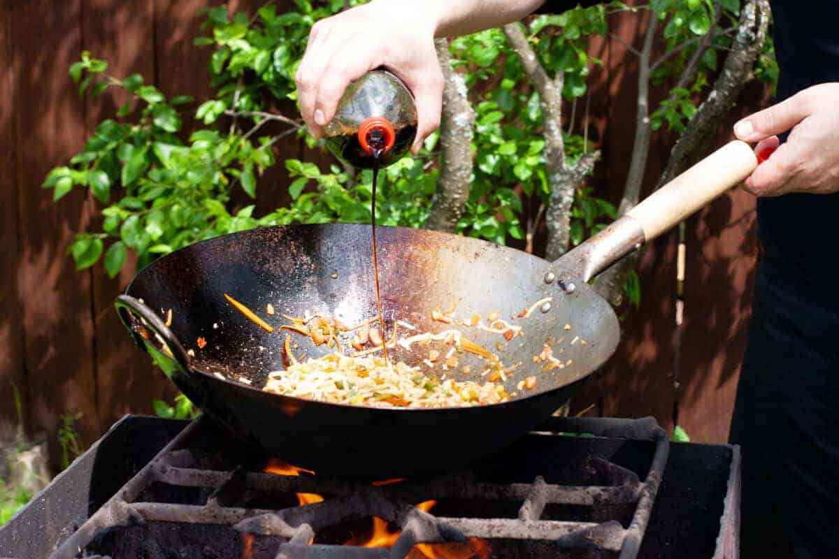 Soy sauce being poured onto a stir-fry, in a wok on a gr.