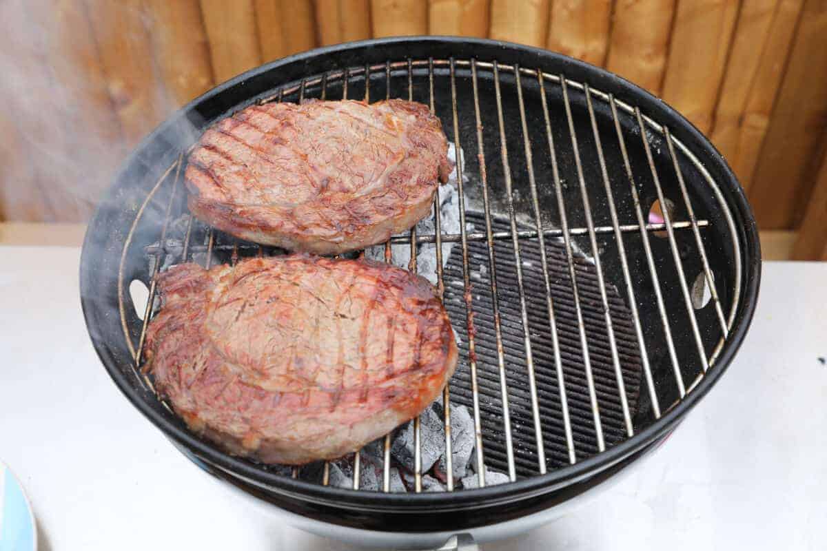 Two steaks grilling on a Weber Smokey Joe 14