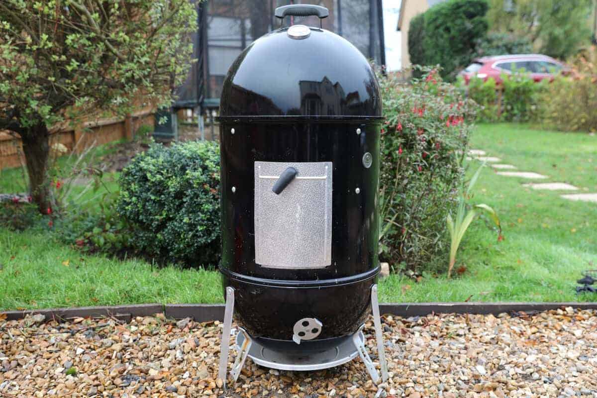 Weber Smokey Mountain smoker in a garden on a gravel path.