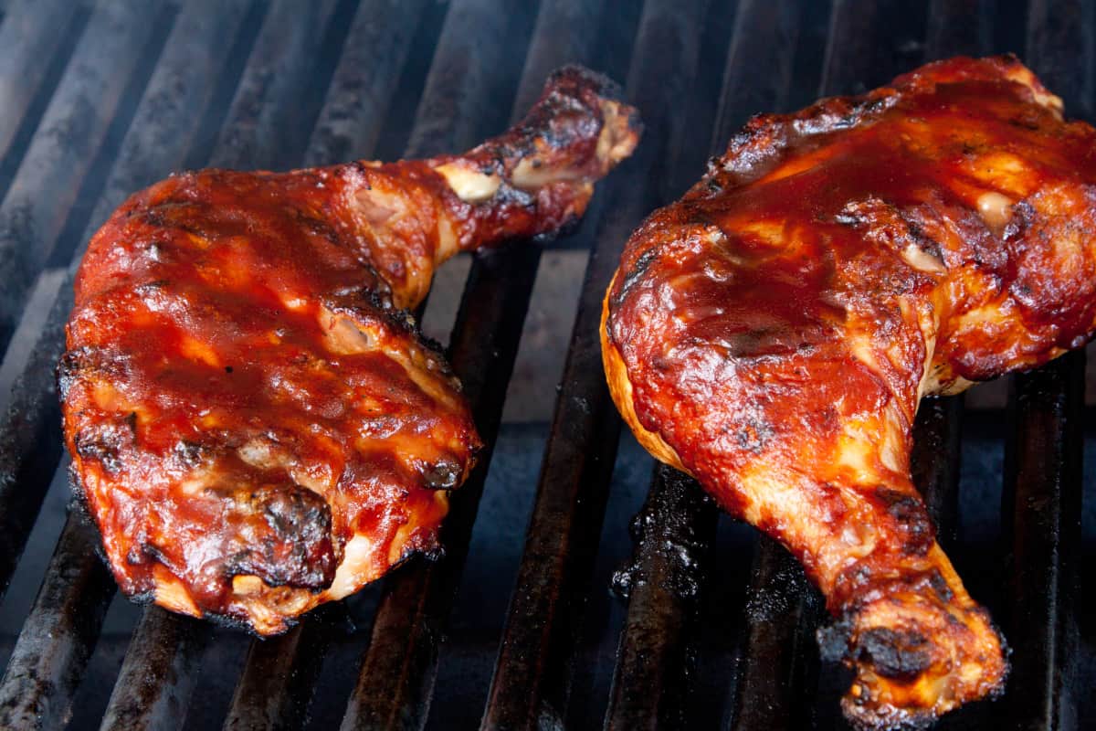Chicken leg quarters on a grill, covered in bbq sa.