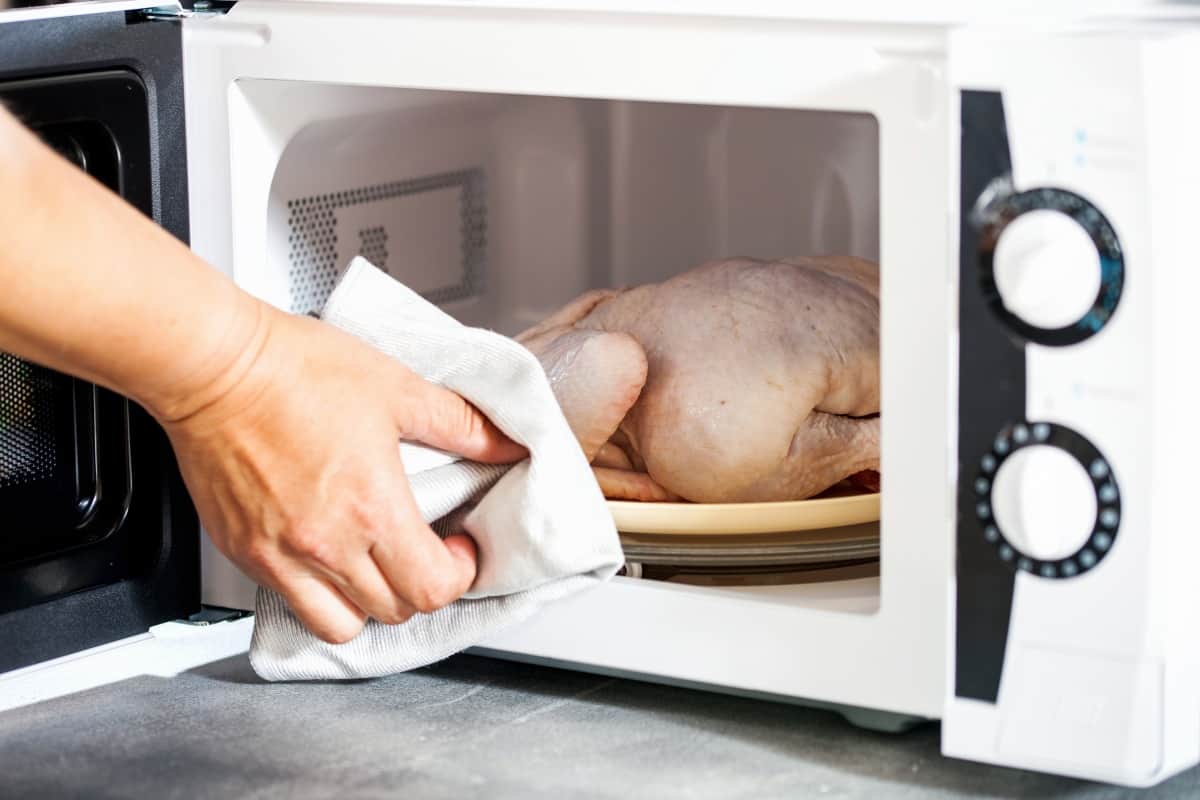 A hand removing a defrosted chicken from a microwave