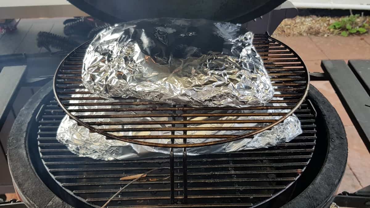 Two foil wrapped briskets on a kamado style smoker