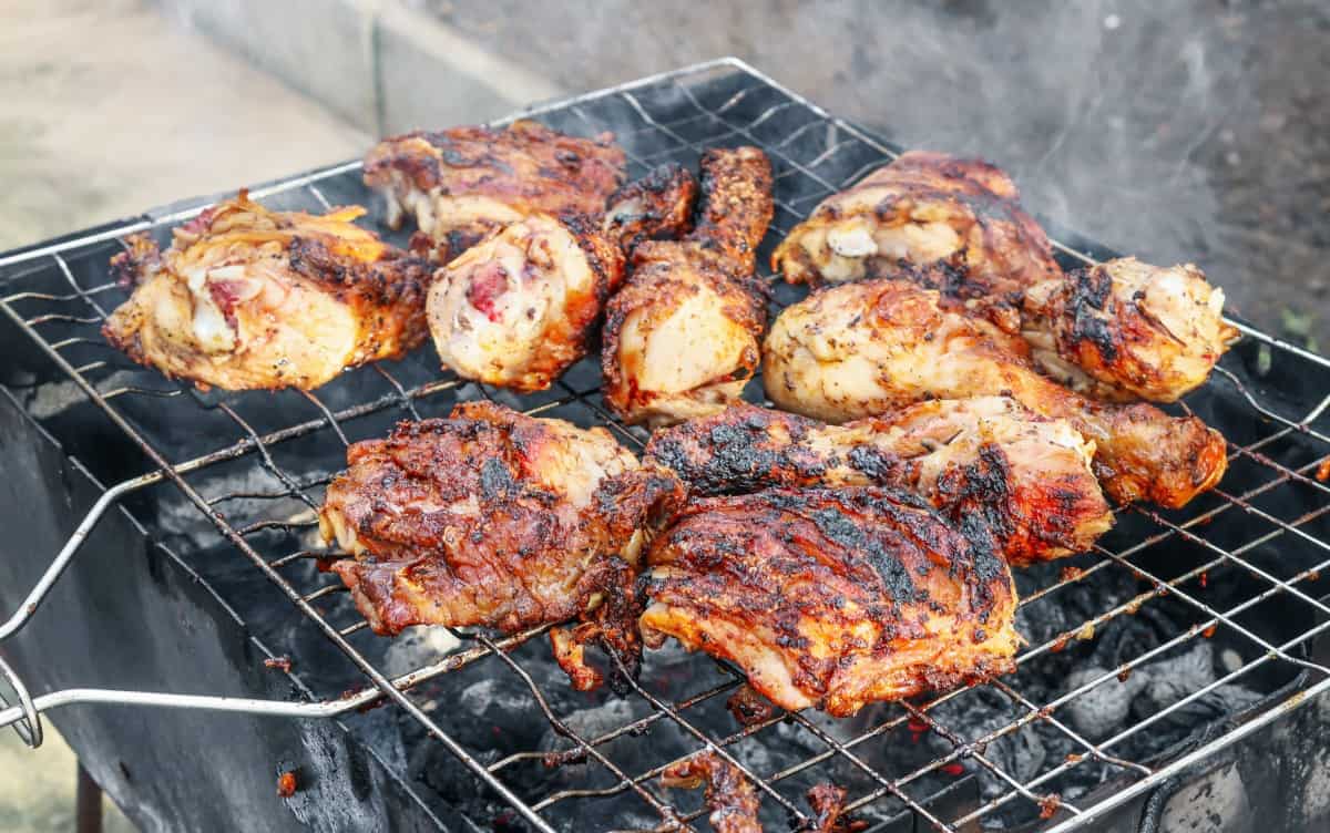 Grilling chicken thighs and drumsticks on an open charcoal gr.