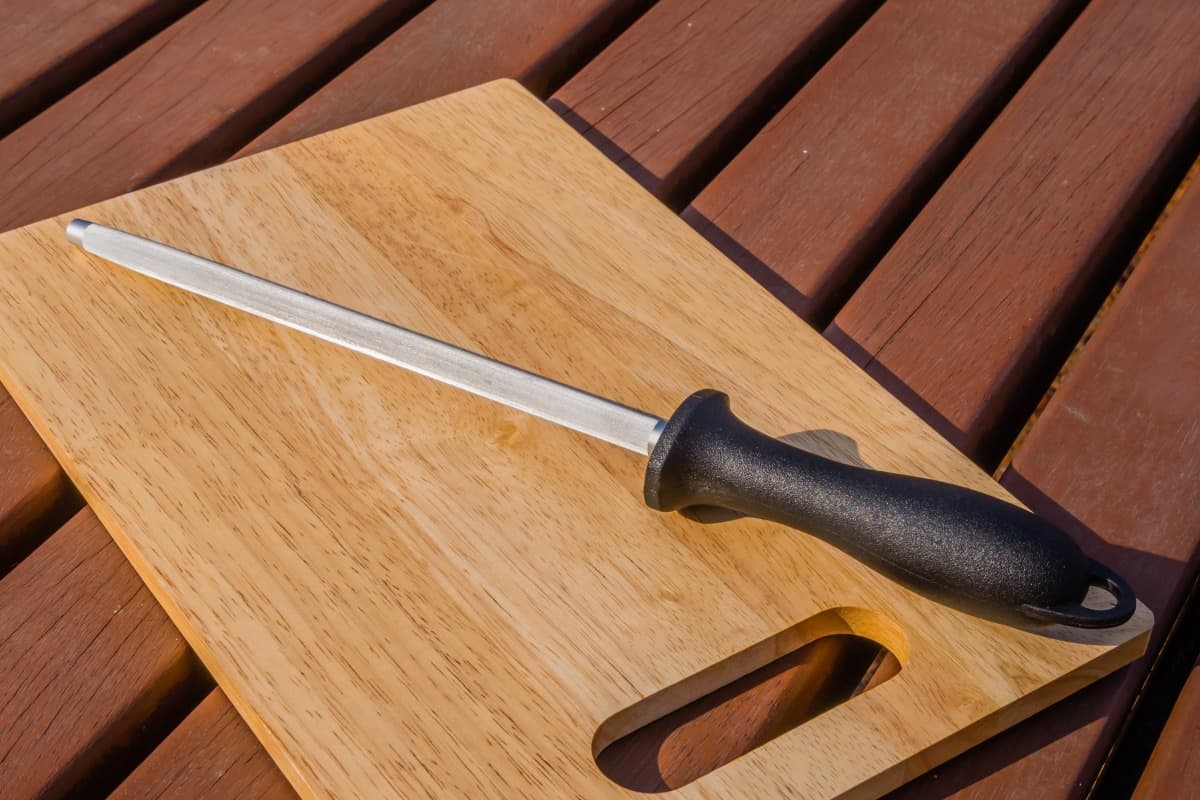 A honing steel on a wooden cutting bo.