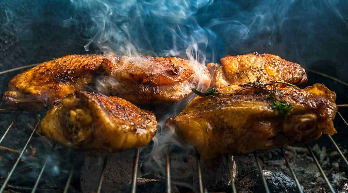 Chicken pieces smoking on a grill.
