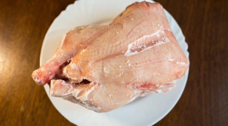 A whole chicken defrosting on a white plate
