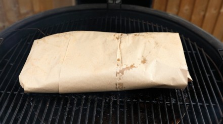 A pink butcher paper wrapped brisket on a kamado style smoker