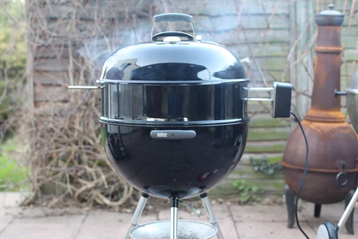 A rotisserie accessory smoking away on a weber kettle, with the lid on.