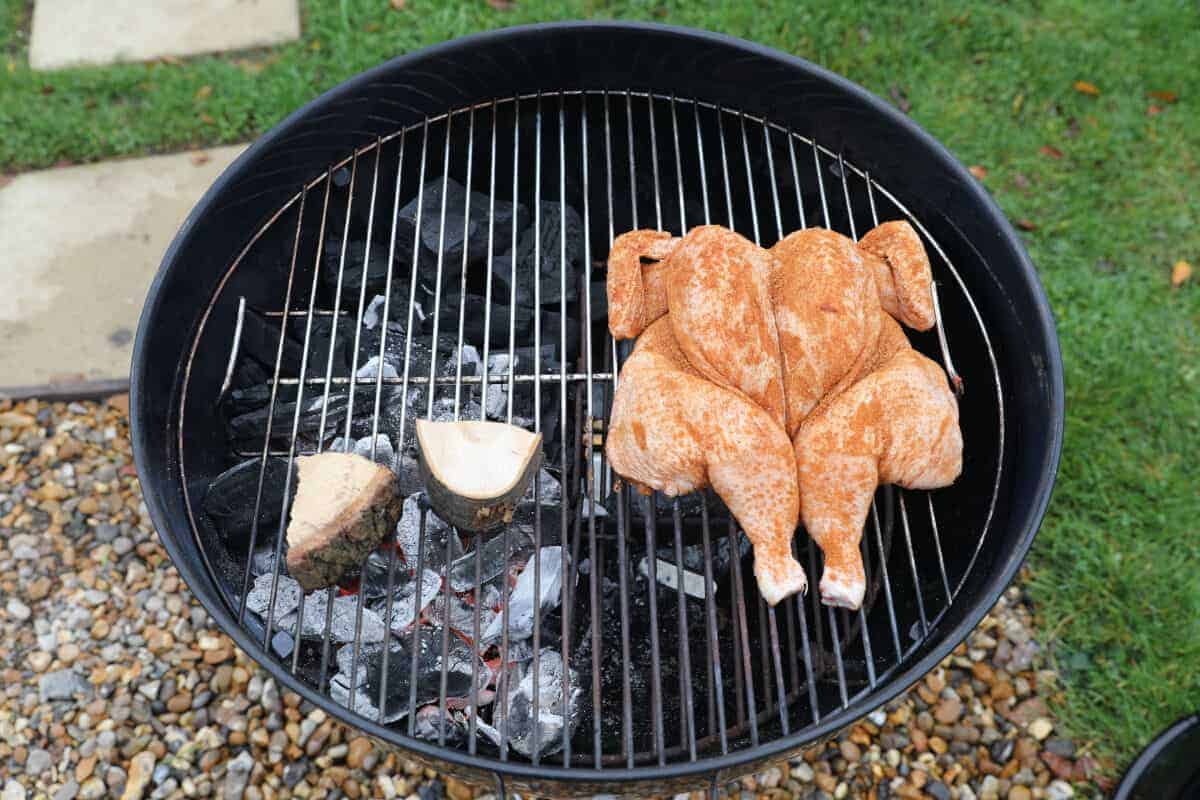 Overhead shot of weber kettle, with a spatchcock chicken and some wood on the gr.