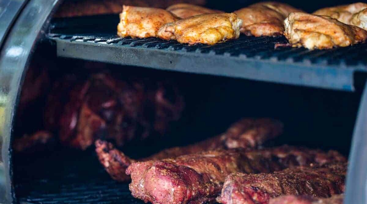 A pellet grill with the lid open, showing various meats being smoked.