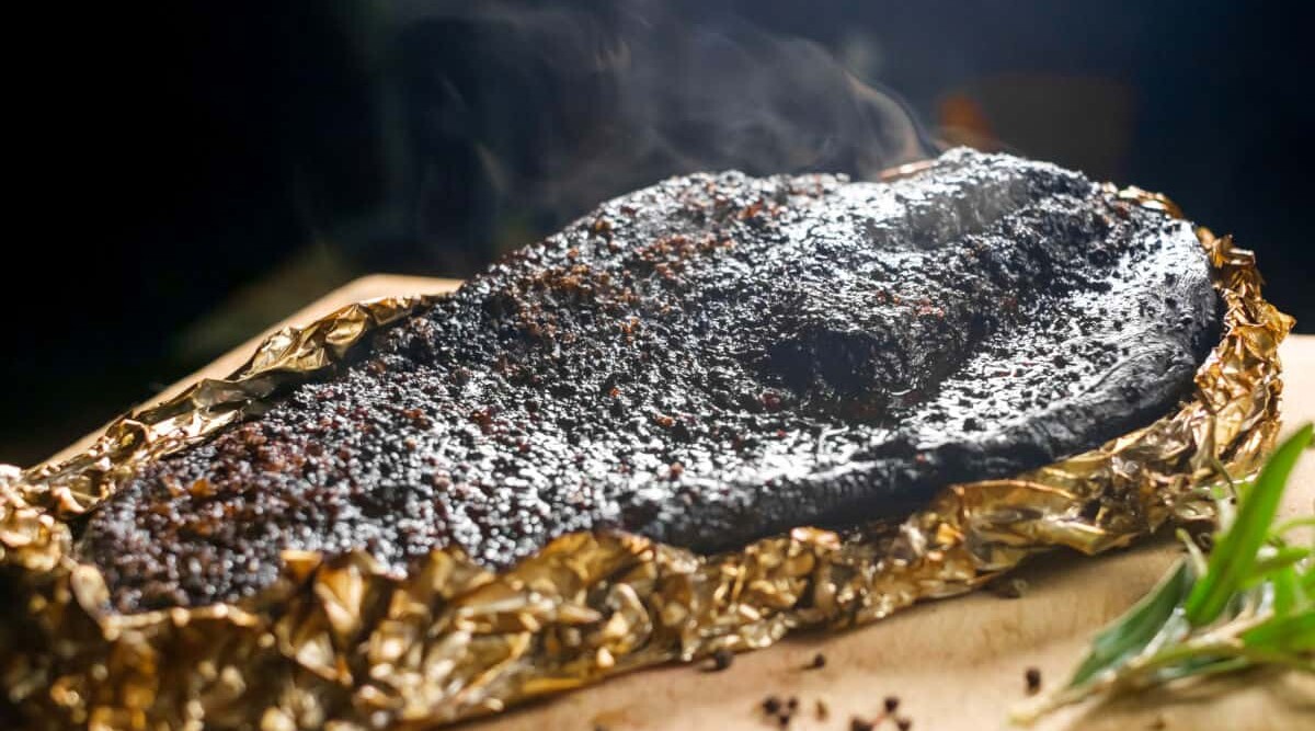 A BBQ smoked brisket half wrapped in foil, steaming after being opened.