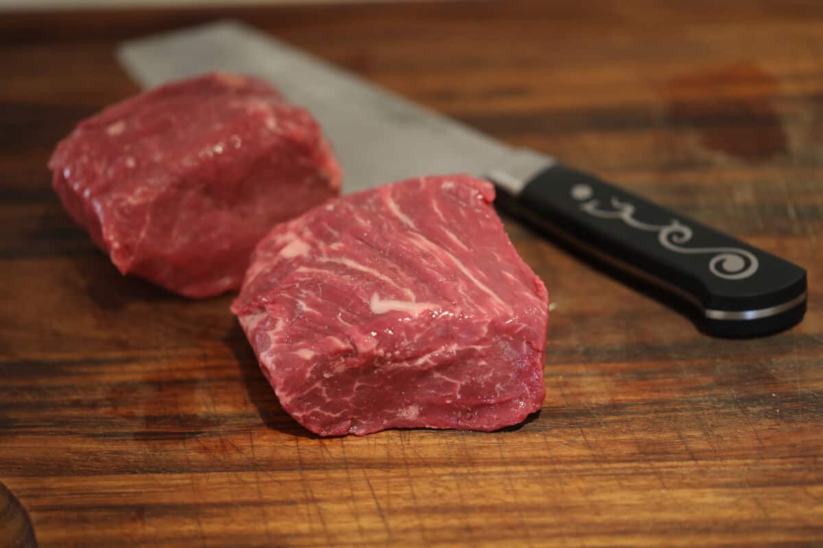 two pieces of Basque beef filet and a japanese knife on a chopping bo.