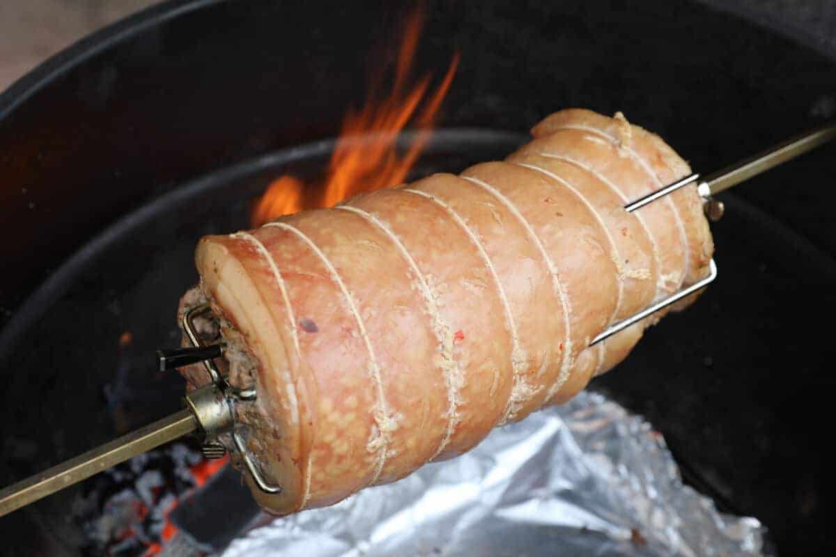 Porchetta on a rotisserie spit with flames in the backgro.