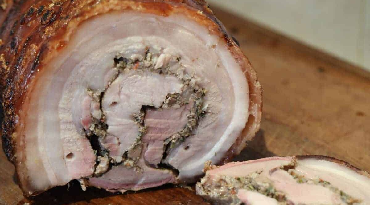 Sliced porchetta on a wooden chopping board.