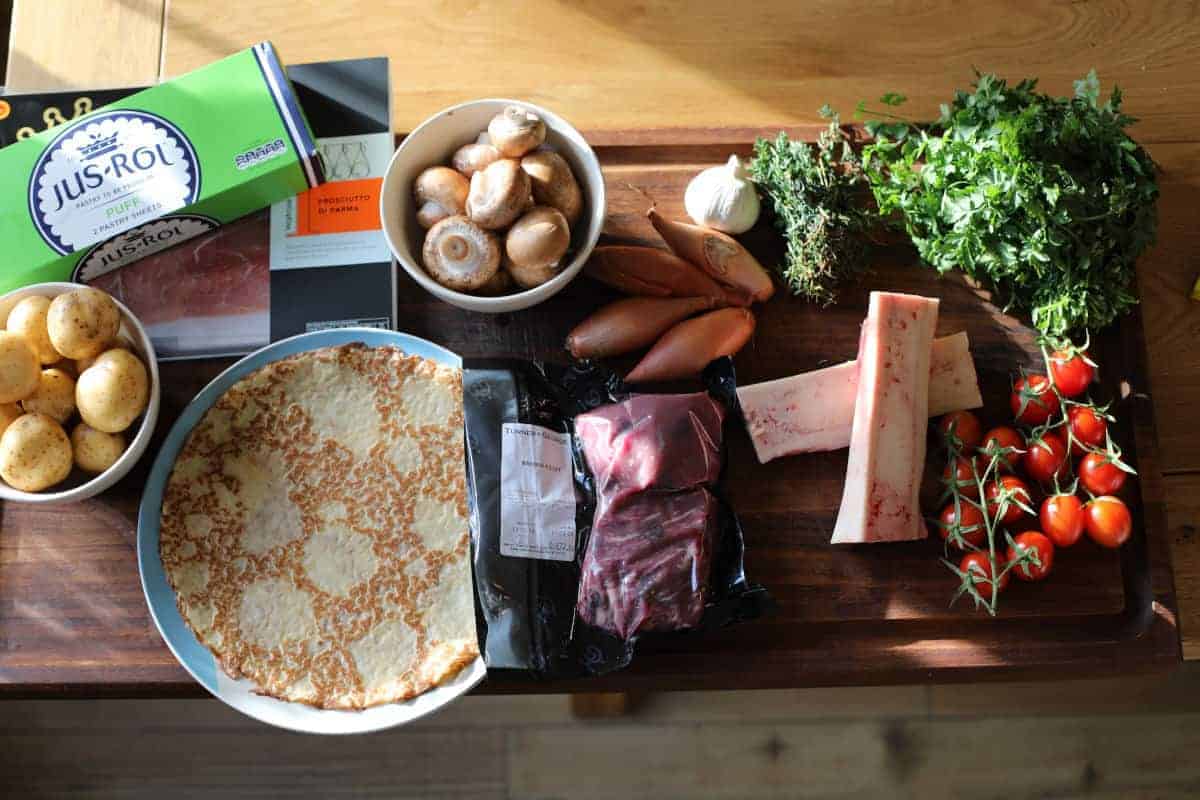 Most of the ingredients required for a beef wellington, laid out on a wooden chopping bo.