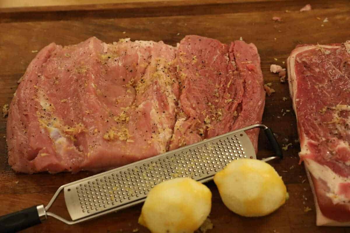 lemon zest, salt and pepper rubbed on pork loin, with 2 lemons and a grater in foreground
