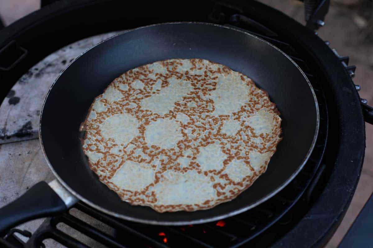 A thin pancake being fried in a pan on a charcoal gr.