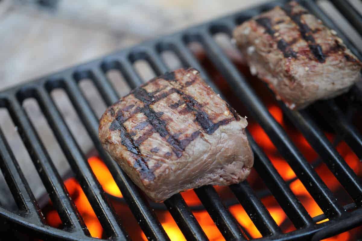 two pieces of beef filet being seared on a charcoal gr.