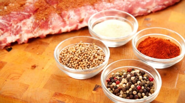Dry rub ingredients and pork ribs on a wooden cutting board.