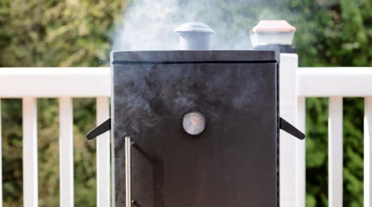 An electric smoker being seasoned, with smoke coming out the top