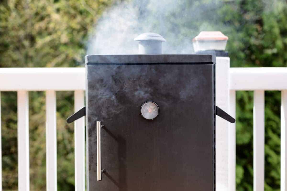 An electric smoker being seasoned, with smoke coming out the top