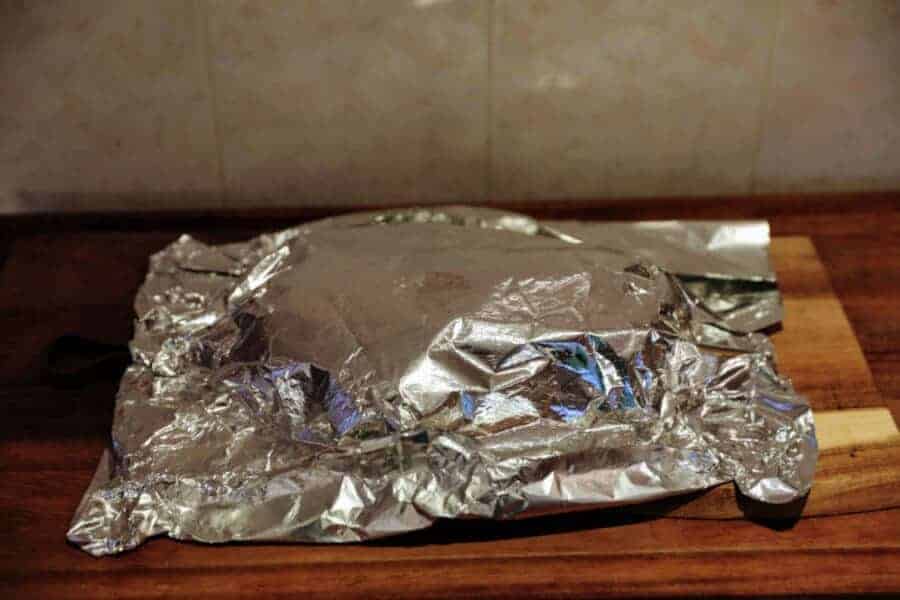 Meat resting in foil on a wooden chopping board