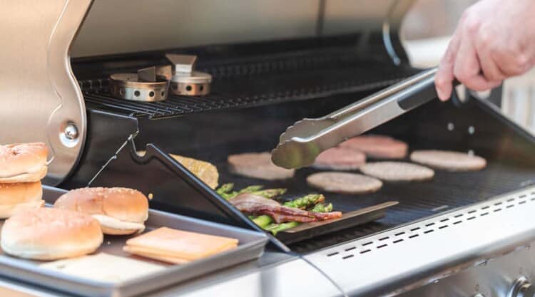 Side view of burgers cooking on a natural gas grill.