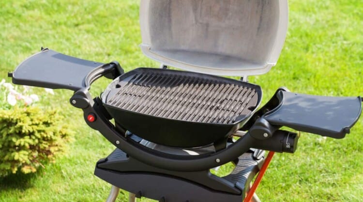 A weber portable gas grill with side tables and lid open on a grass field