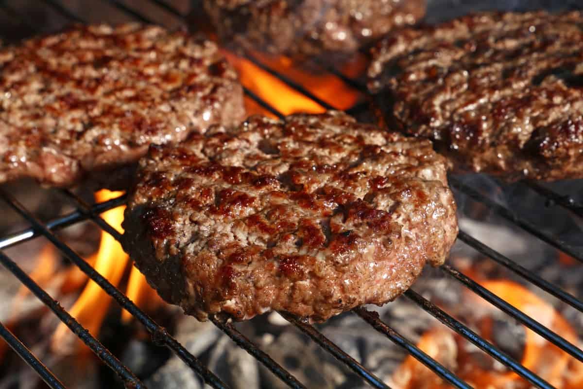 Burgers on a grate over a flaming hot grill
