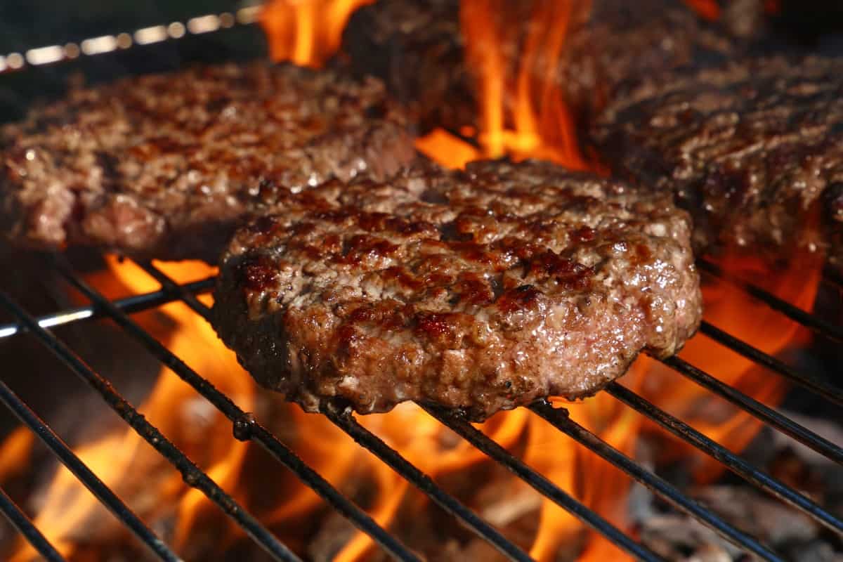 burgers cooking on a hot flaming charcoal gr.