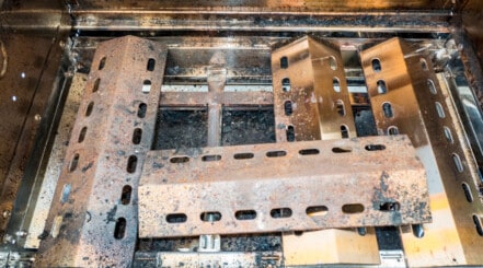 Close up of dirty and rusted gas grill burners and flavorizer bars.