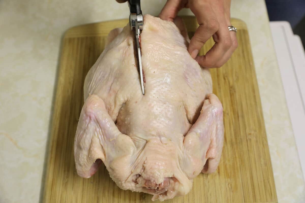 Chicken on cutting board with backbone being cut with kitchen shears