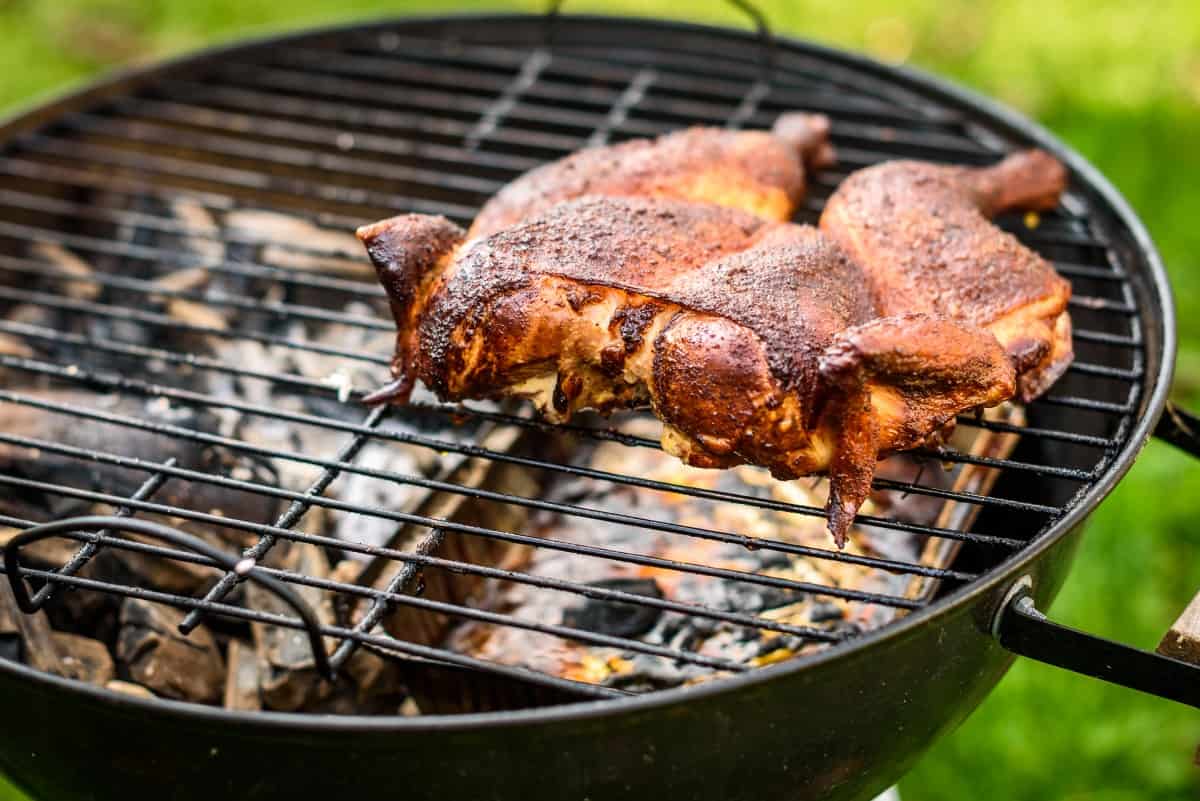 A spatchcock chicken on a charcoal grill with foil pan underneath