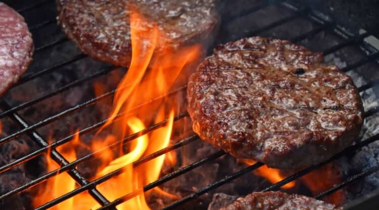 Burgers searing on a grill with flames licking the underside.