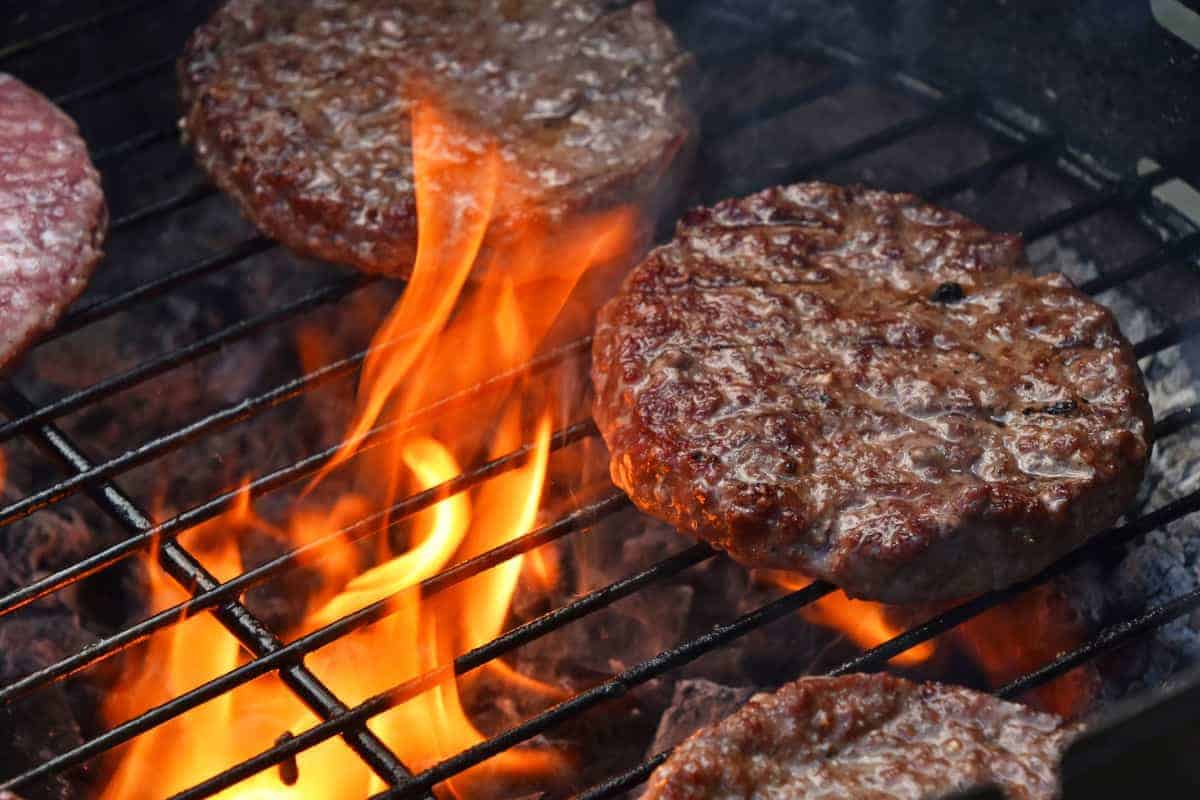 Burgers searing on a grill with flames licking the unders.