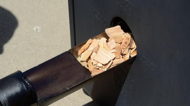 Wood chips being added into an electric smoker via side opening.