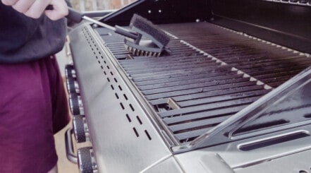 A gas grill being cleaned with a reversible grill brush