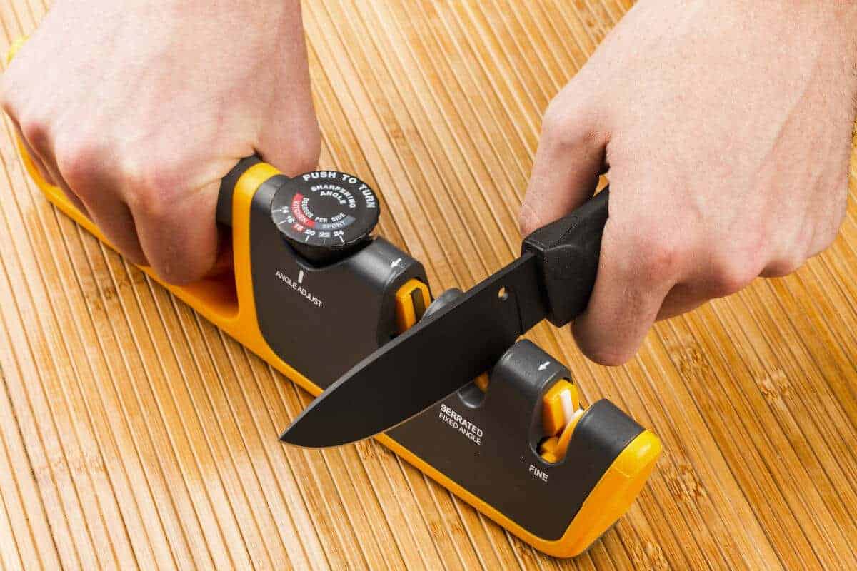 Close up of a man pulling a knife through an adjustable manual knife sharpe.