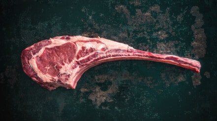 A tomahawk steak on a black surface