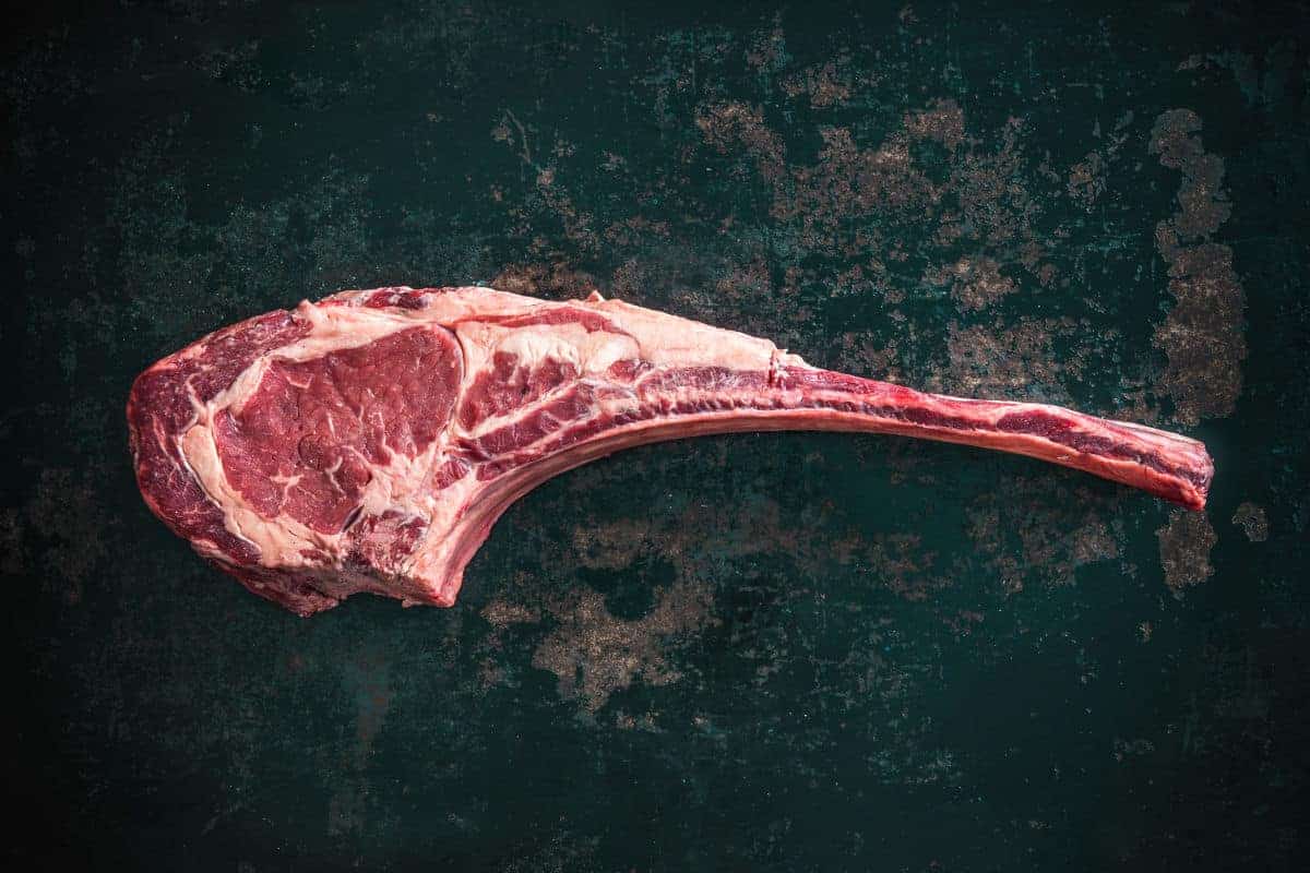 Close up of a tomahawk steak on a dark, slate like looking surf.